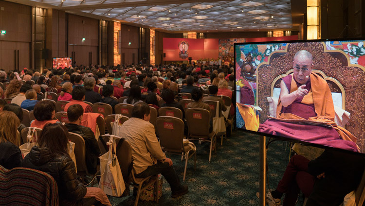 La gente en el fondo del salón viendo a Su Santidad el Dalái Lama en las pantallas de televisión durante su enseñanza en Delhi, India, el 25 de diciembre de 2016. Foto/Tenzin Choejor/OHHDL