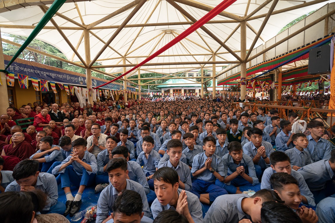 Jóvenes estudiantes tibetanos sentados en el patio principal del Tíbet viendo la Ceremonia de Ofrenda de Larga Vida para Su Santidad el Dalái Lama en pantallas gigantes en Dharamsala, HP, India, el 17 de mayo de 2019. Foto de Tenzin Choejor